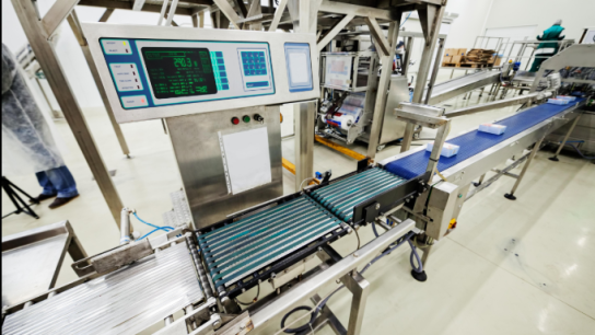 Check weigher otomatis sedang menimbang produk di atas konveyor untuk memastikan akurasi berat pada lini produksi